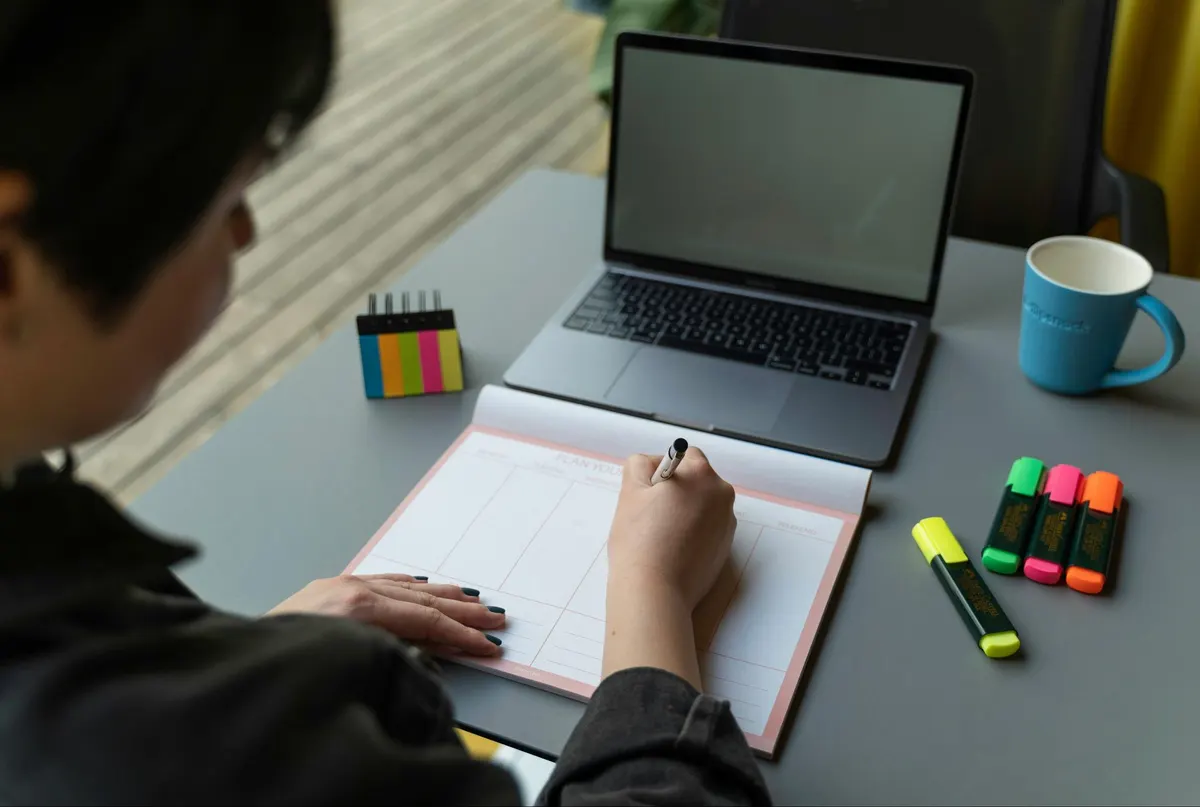 Taking notes in a planner next to a laptop